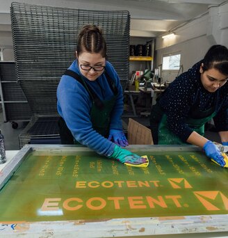 Workers screen-printing the Ecotent® logo onto tent fabric.